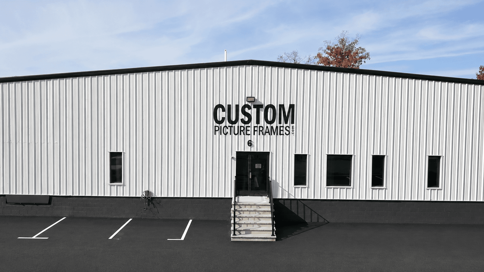 The CustomPictureFrames.com workshop and showroom at 6 Shirley Avenue in Somerset, New Jersey, a white industrial building with the company logo across the front and customer parking out front