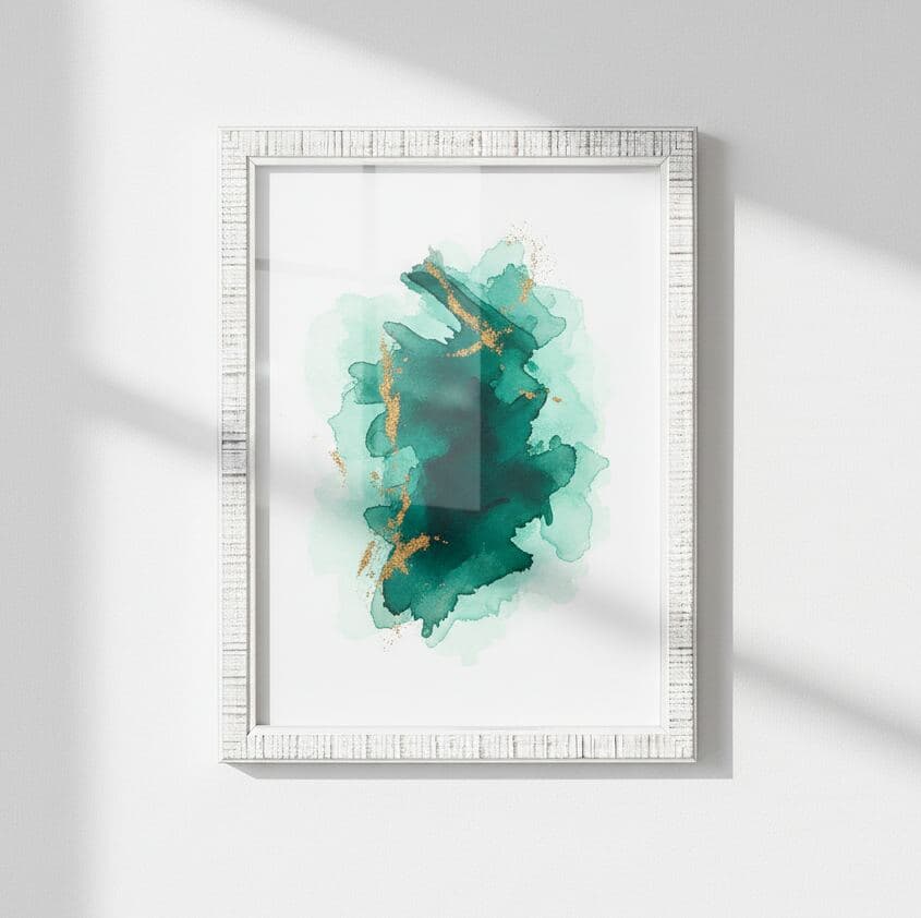 Textured white picture frame hangs on white wall displaying watercolor painting in deep green and gold hues illuminated by natural sunlight