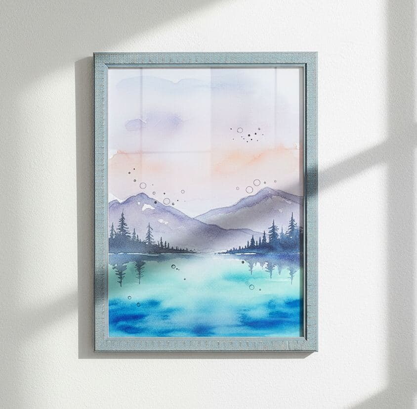 Blue-washed wood picture frame hangs on white wall displaying watercolor painting of mountains and lake in soft pastel hues
