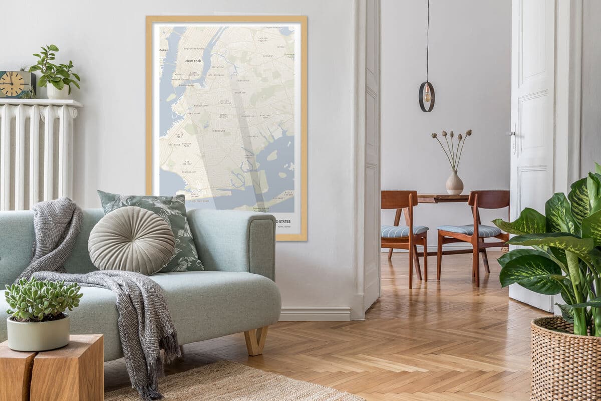 Framed city map print in Natural Wood frame hangs above light gray sofa with cushions and throw blanket in bright living room adjoining dining area
