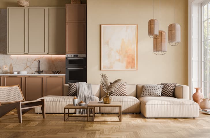 Natural Wood frame with abstract painting in warm orange tones hangs above cream sectional sofa in modern living room adjoining kitchen with tan cabinets