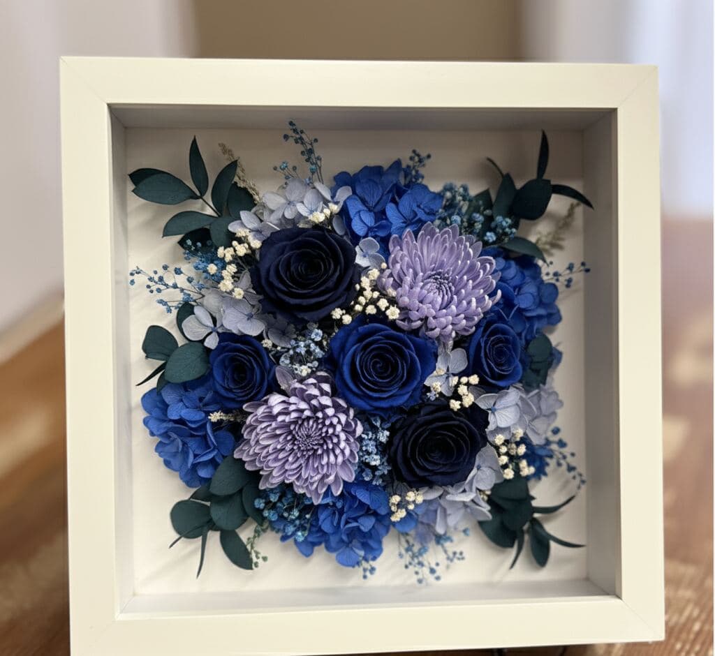 Bright white shadowbox picture frame with 0.75 inch moulding width displaying preserved wedding or special occasion flower bouquet with navy blue roses purple chrysanthemums and eucalyptus utilizing 0.875 inch depth for floral preservation bouquet displays and dimensional flower picture frames with gallery-quality presentation