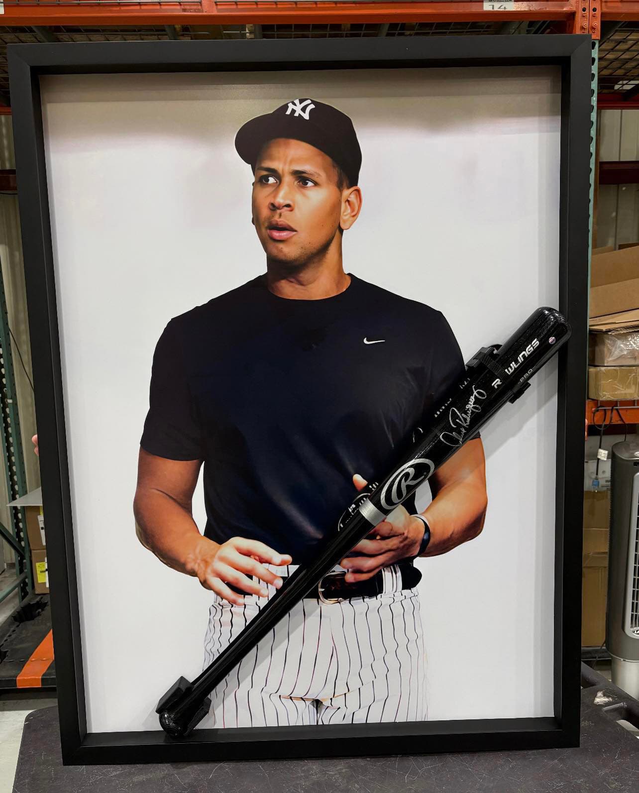 Oversized framed portrait of Alex Rodriguez in a Yankees cap and pinstripes holding a signed black Rawlings game bat across his torso, finished in a deep black moulding