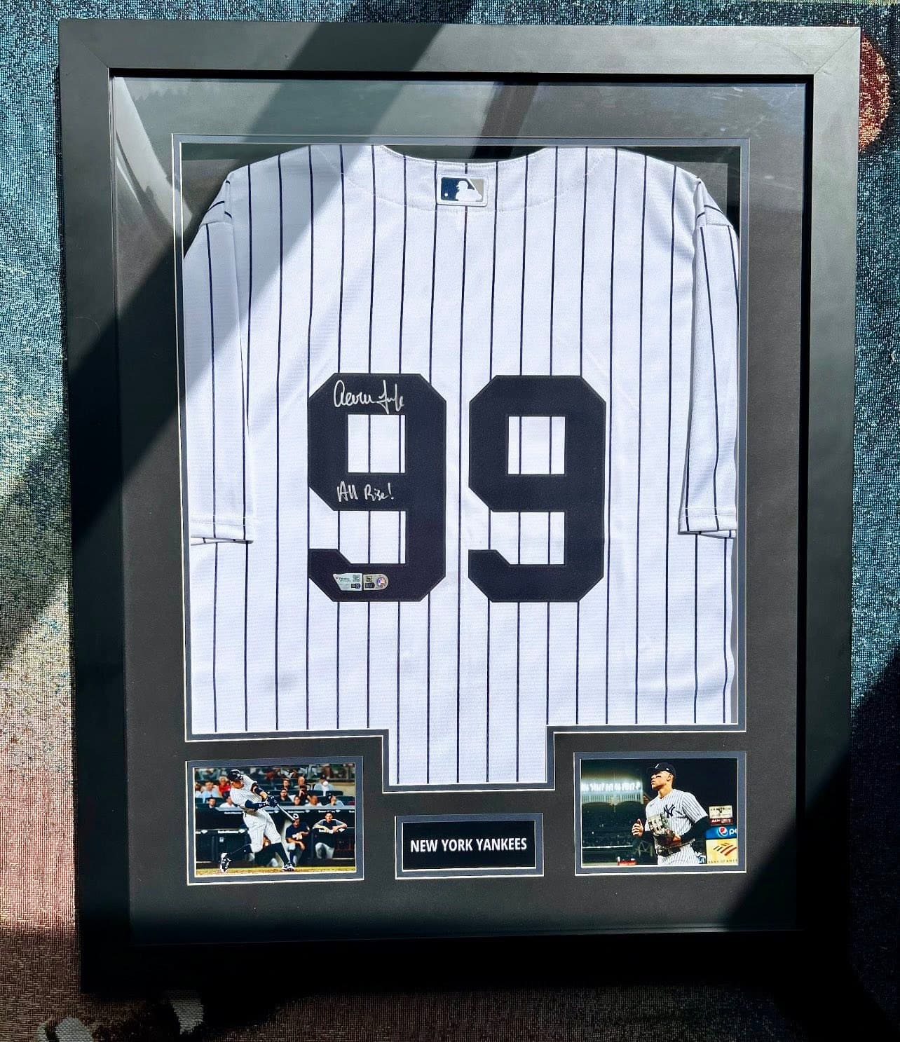 Signed Aaron Judge New York Yankees #99 home pinstripe jersey inscribed 'All Rise!' framed in a black shadow box with twin action shots (batting follow-through and on-field portrait) and an engraved 'New York Yankees' nameplate