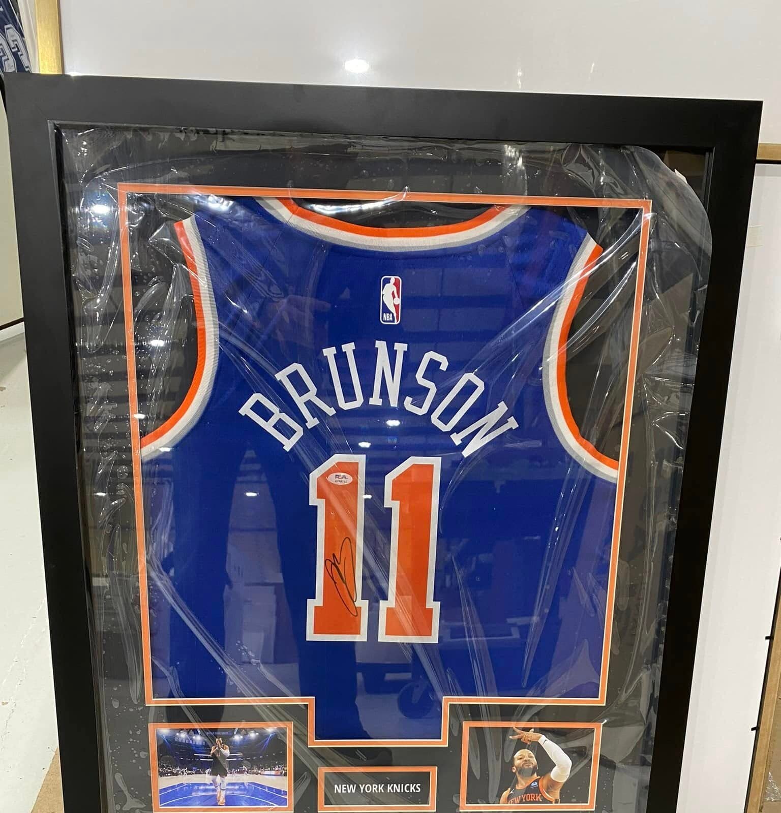 Autographed Jalen Brunson New York Knicks #11 jersey framed in a shadow box with orange double mat, twin action shots, and 'New York Knicks' nameplate