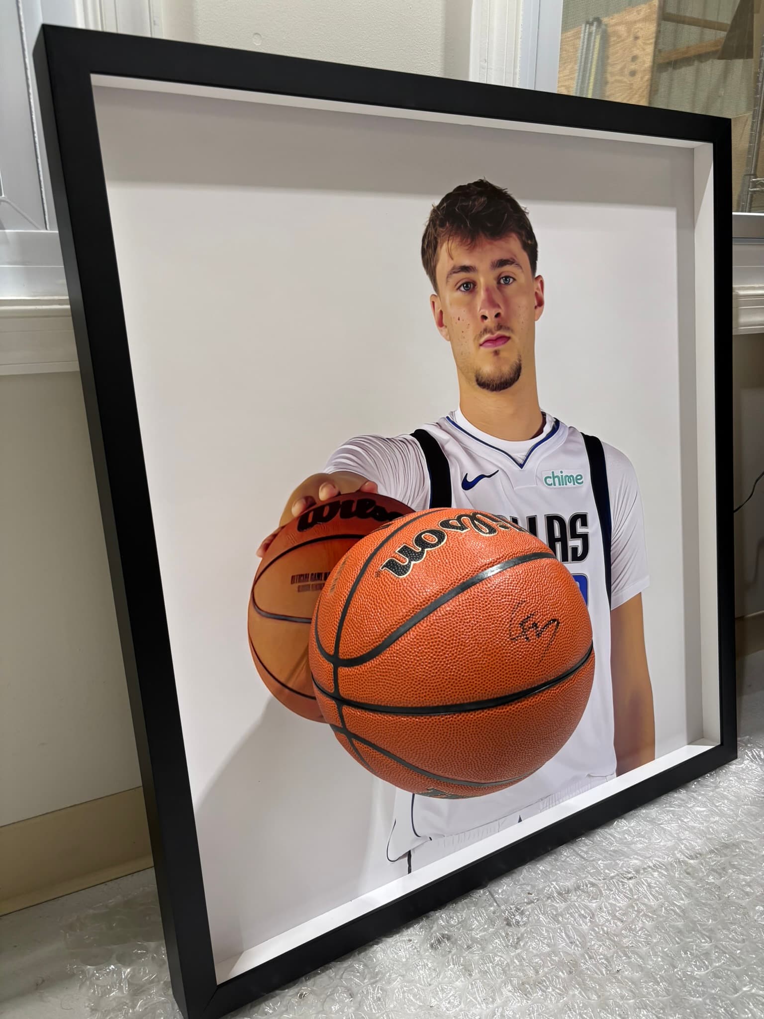 Signed Wilson basketball mounted in front of a large Dallas Mavericks player portrait, framed in a deep black shadow box with white interior backing