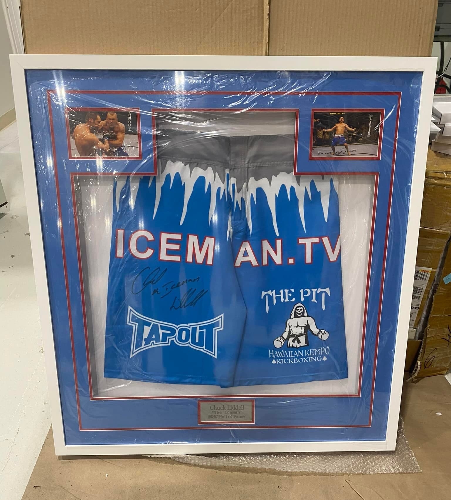 Signed Chuck 'The Iceman' Liddell blue TapouT fight trunks framed in a white moulding with blue double mat, twin octagon action photos, and 'Chuck Liddell - UFC Hall of Fame' nameplate