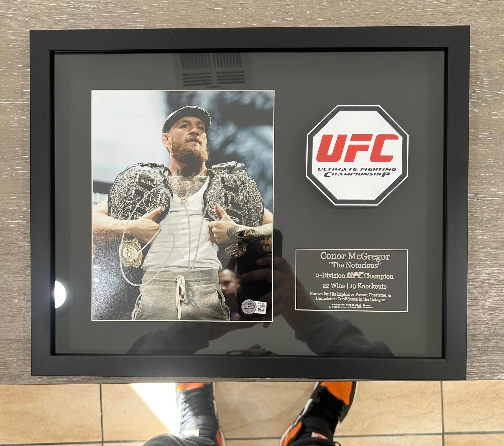 Signed Conor McGregor 'The Notorious' two-belt photo framed in a deep black shadow box with embroidered UFC octagon patch and engraved tribute nameplate