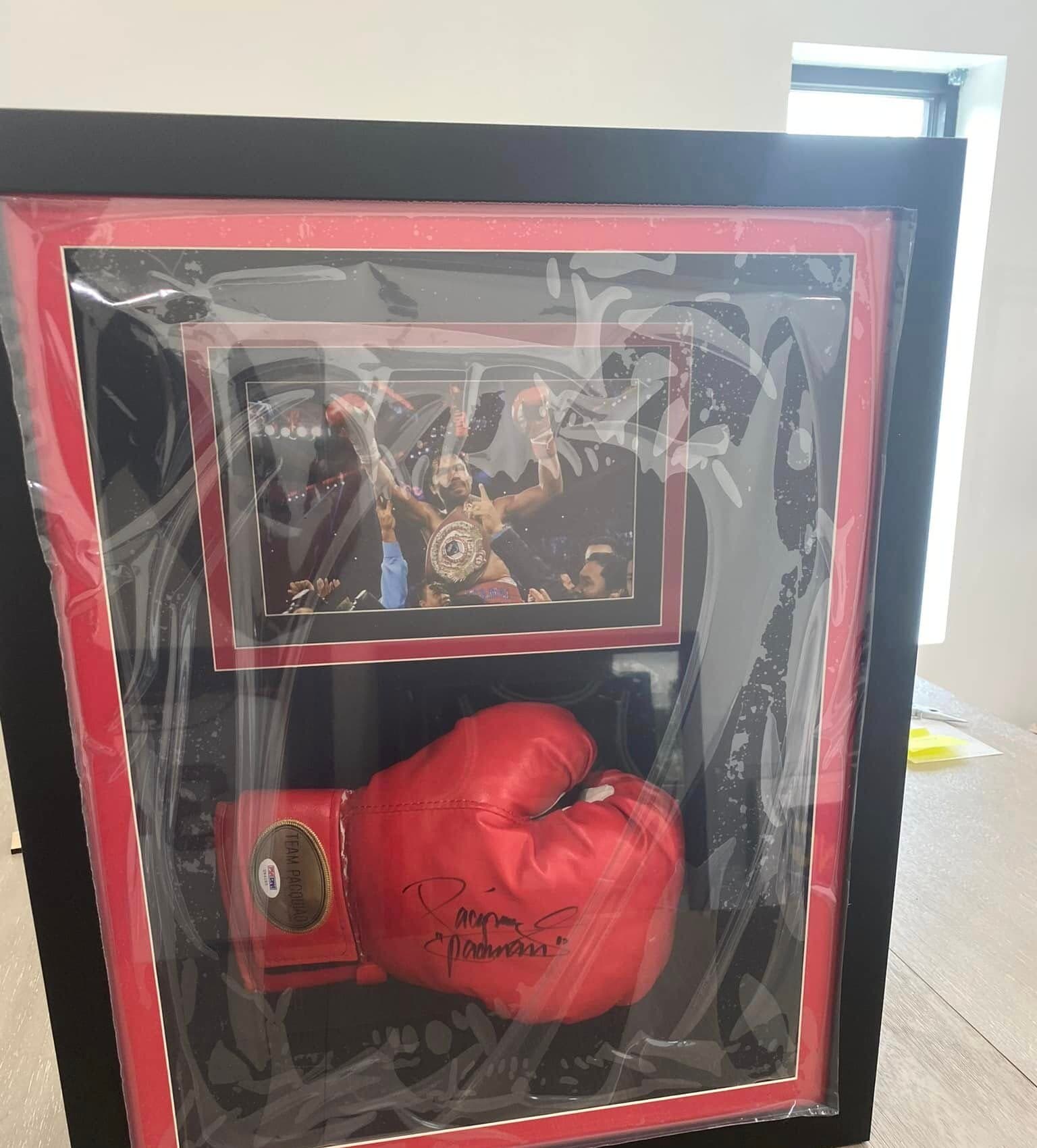 Signed Manny Pacquiao red Team Pacquiao boxing glove framed in a deep black shadow box with red double mat, splatter-pattern accents, and a title-win celebration action photo above the glove