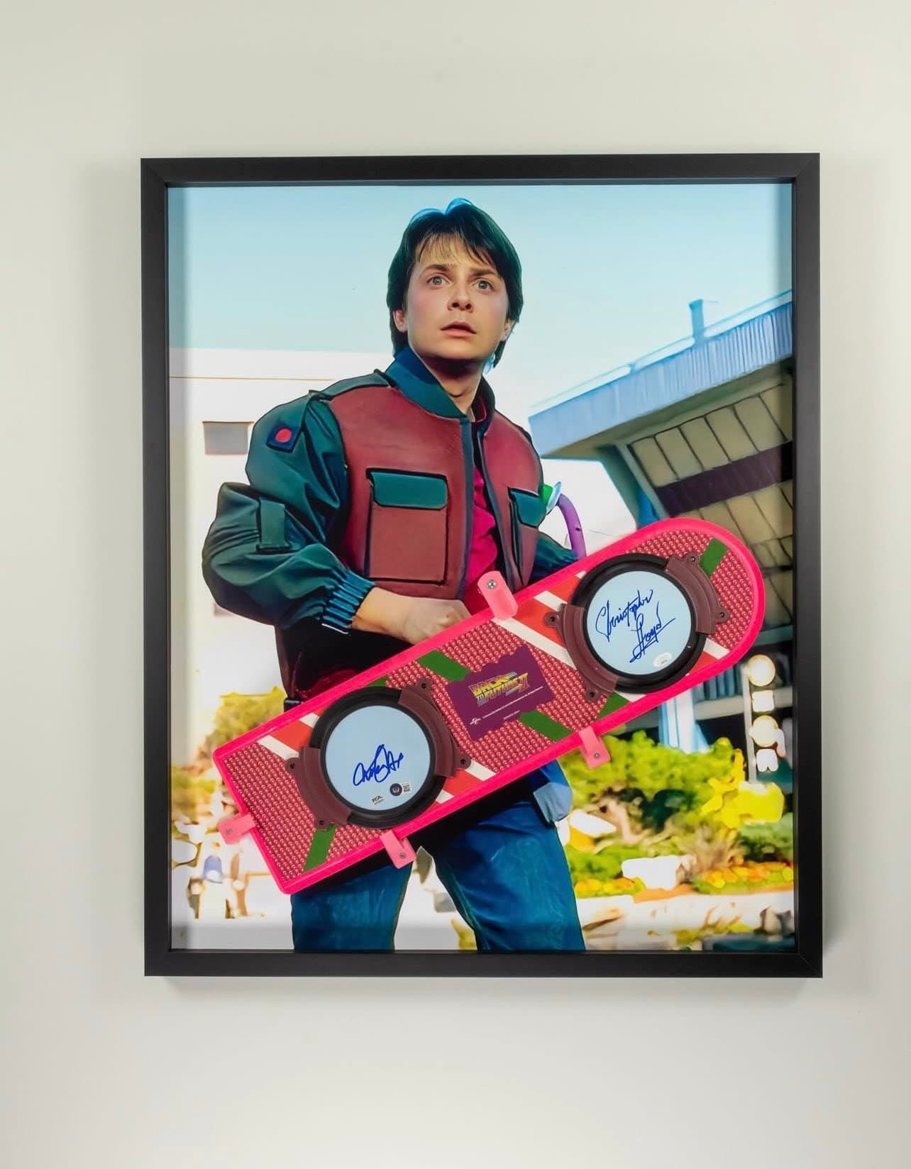 Custom Back to the Future Part II pink Mattel hoverboard framed in a deep black shadow box with a Marty McFly futuristic-outfit movie still alongside the prop