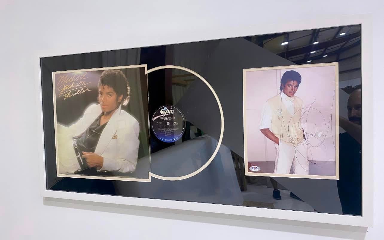PSA-authenticated signed Michael Jackson Thriller LP framed in a white moulding with the album jacket on the left, the Epic-label vinyl spinning at center, and a signed Thriller-era promotional photo on the right
