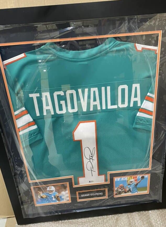 Sports memorabilia shadow box framing example: autographed Tua Tagovailoa Dolphins jersey mounted with action prints in deep shadow box